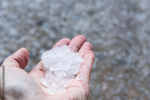 Woman is holding pieces ice crystals of hail in springtime after hail storm, defocused ice background