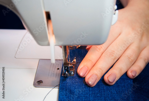 seamstress's hands sew blue jeans on the machine