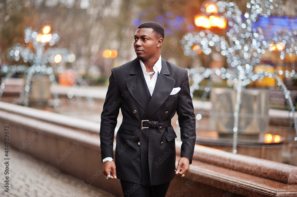 Portrait of young and handsome african american businessman in suit walking on cemter of city with garlands.