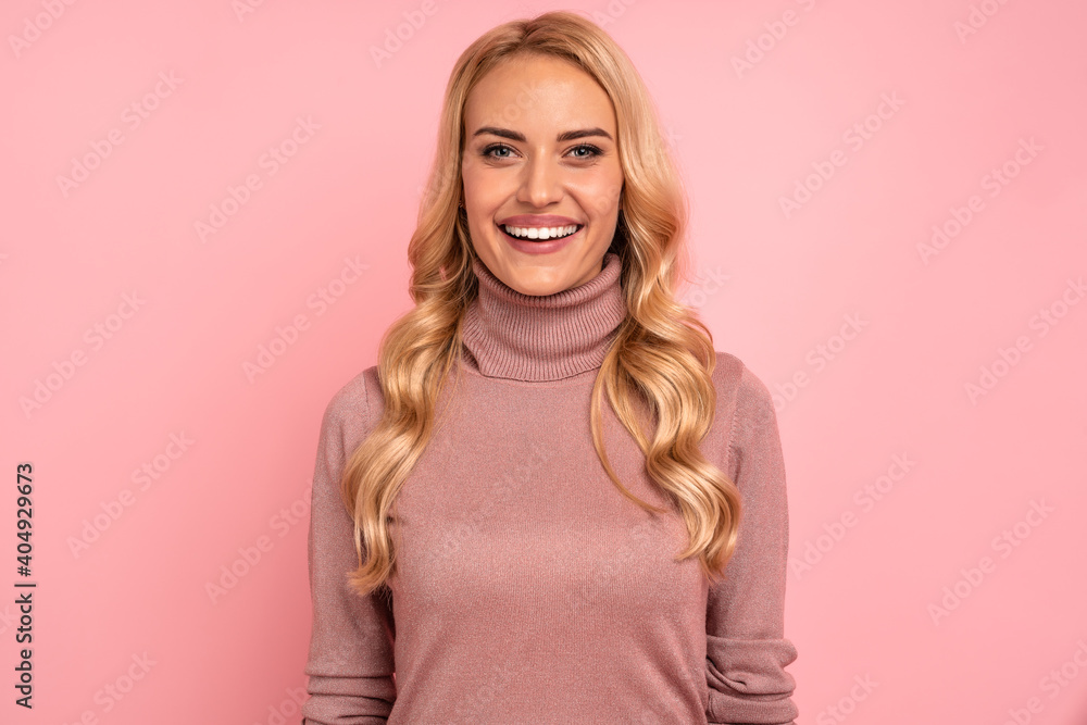 Smiling blonde woman in sweater posing at the camera over pink background Smiling blonde woman in sweater posing at the camera over pink background