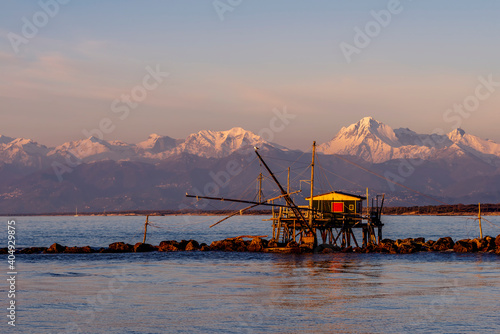 Drop net fishing hut at sunset against the Alps covered with snow, Marina di Pisa, Tuscany, Italy photo