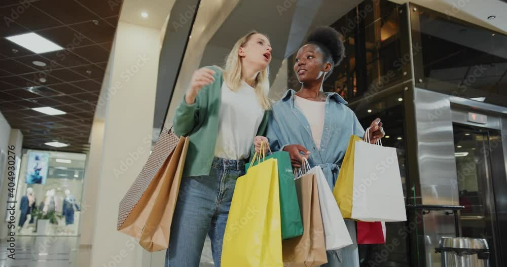 Happy caucasian and afro-american girls best friends gathering in shopping mall searching and buying stylish clothes together. Happy caucasian and afro-american girls best friends gathering in shopping mall searching and buying stylish clothes together.