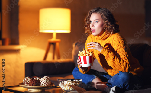 Young female eating French fries and watching interesting movie