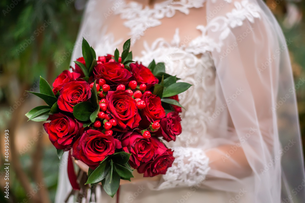 Fototapeta premium Wedding bouquet with red flowers in the hands of the bride. Bouquet with red berries and roses close-up.