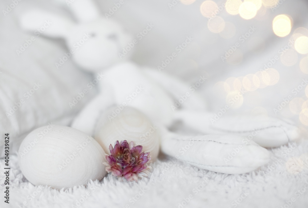 Easter funny white stuffed rabbit toy on a white bed with wooden eggs zero west. Easter funny white stuffed rabbit toy on a white bed with wooden eggs zero west.