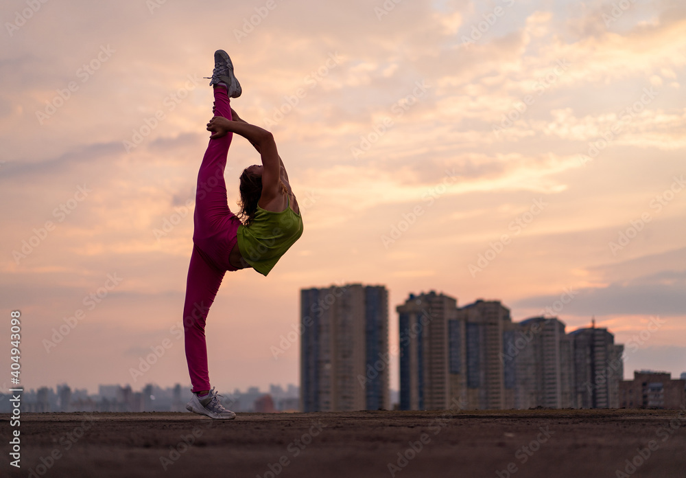 Flexible woman doing split outdoor on the dramatic sunset background. Concept of yoga, healthy lifestyle and stretching