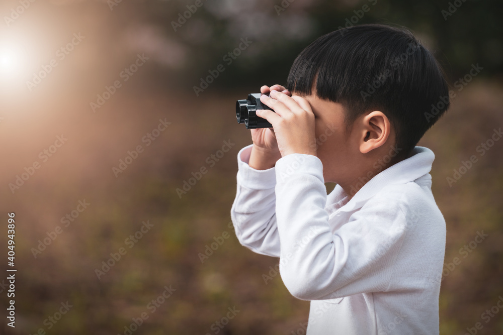 Little Asian boy looking through binoculars in the forest. The child was watching binoculars in nature outdoor. Little Asian boy looking through binoculars in the forest. The child was watching binoculars in nature outdoor.