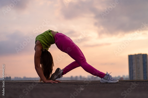 Flexible woman doing poses outdoor on the dramatic sunset background. Concept of activity, healthy lifestyle and wellness 