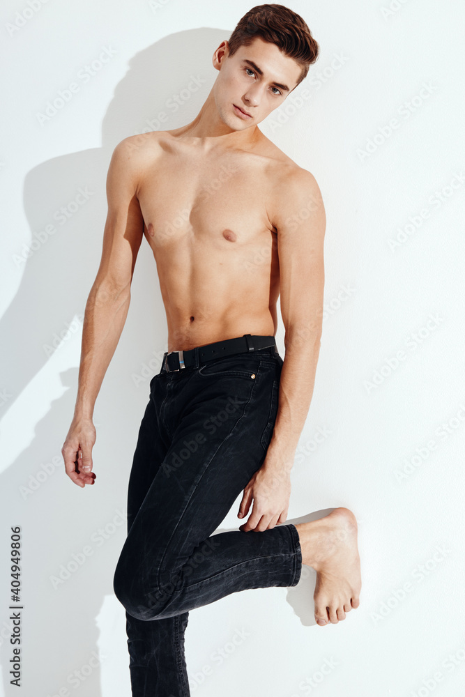 Fototapeta premium Handsome guy with a naked torso stands on one leg against the wall