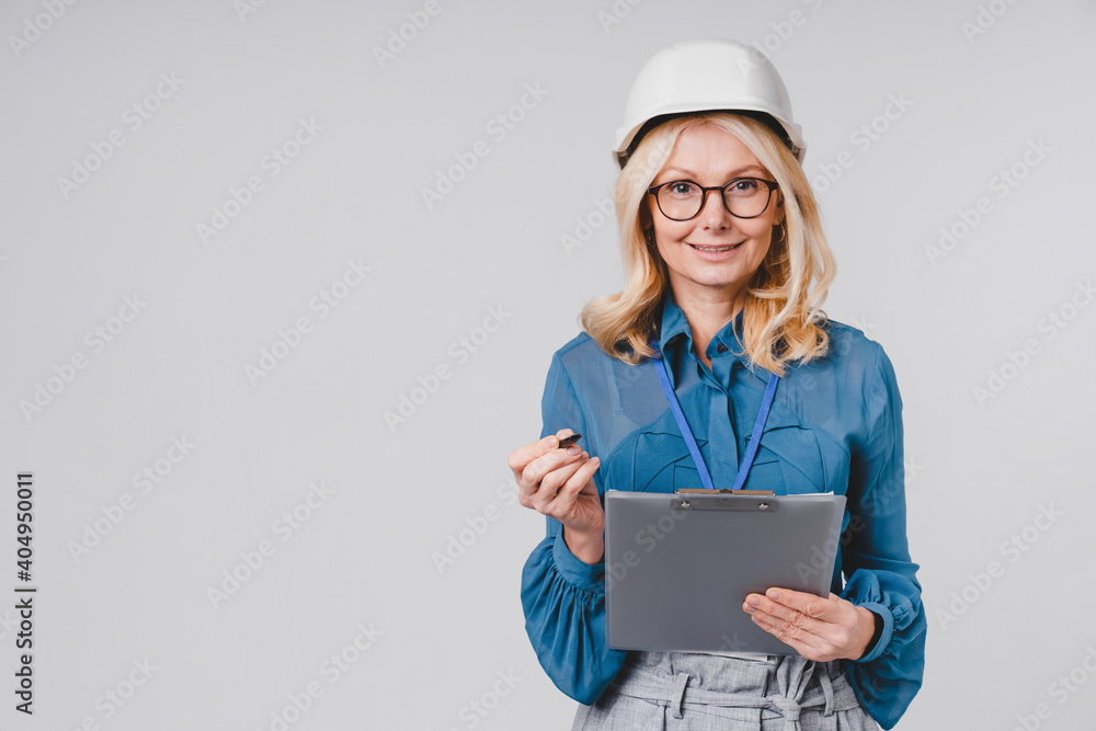 Attractive middle-aged caucasian woman engineer with hard hat and clipboard isolated over grey background Attractive middle-aged caucasian woman engineer with hard hat and clipboard isolated over grey background