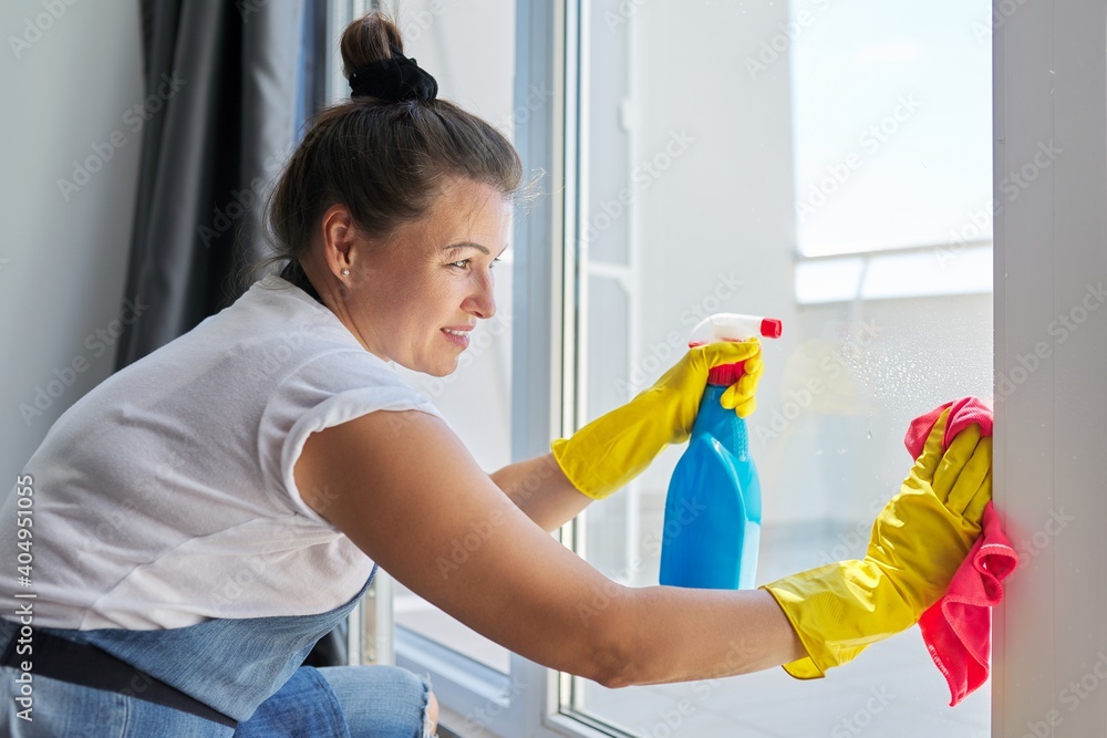 House cleaning, mature woman in rubber gloves wearing an apron washing windows House cleaning, mature woman in rubber gloves wearing an apron washing windows