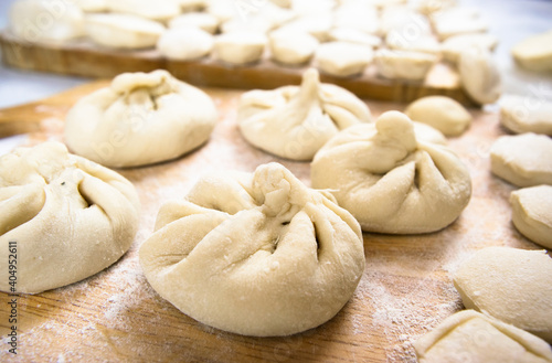 Handmade khinkali dumplings and ravioli are beautifully arranged in rows on a cutting board and sprinkled with flour. Close-up, macro.