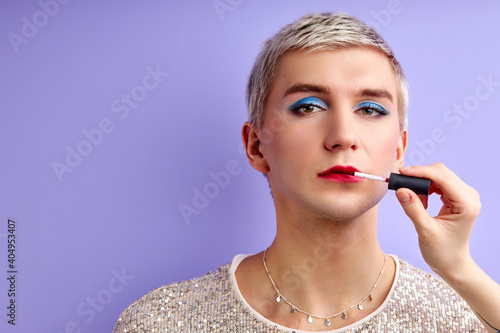 Obraz na płótnie effeminate man applying red lipstick on his lips isolated on purple background