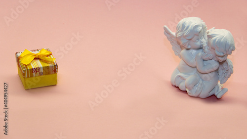 valentine s day gift in a box with a yellow bow and kissing angels on a pink background