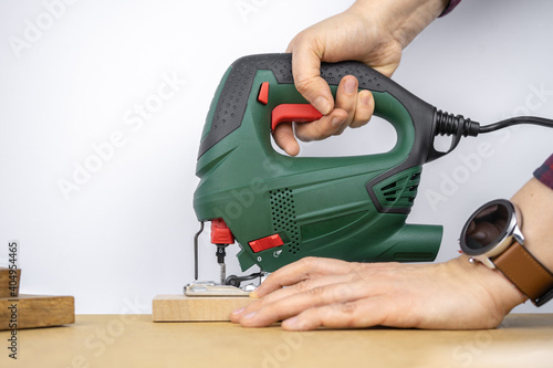 Modern electric jig saw tool in a hand for DIY home woodworking. Wood boards on background