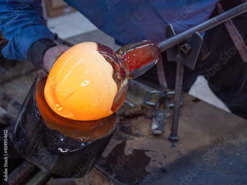 Artisan hands working with hot malleable glass on glassblower whistle.