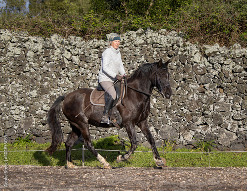 Woman riding a black Lusitano horse outdoors, good weather, Azores. © Ayla Harbich