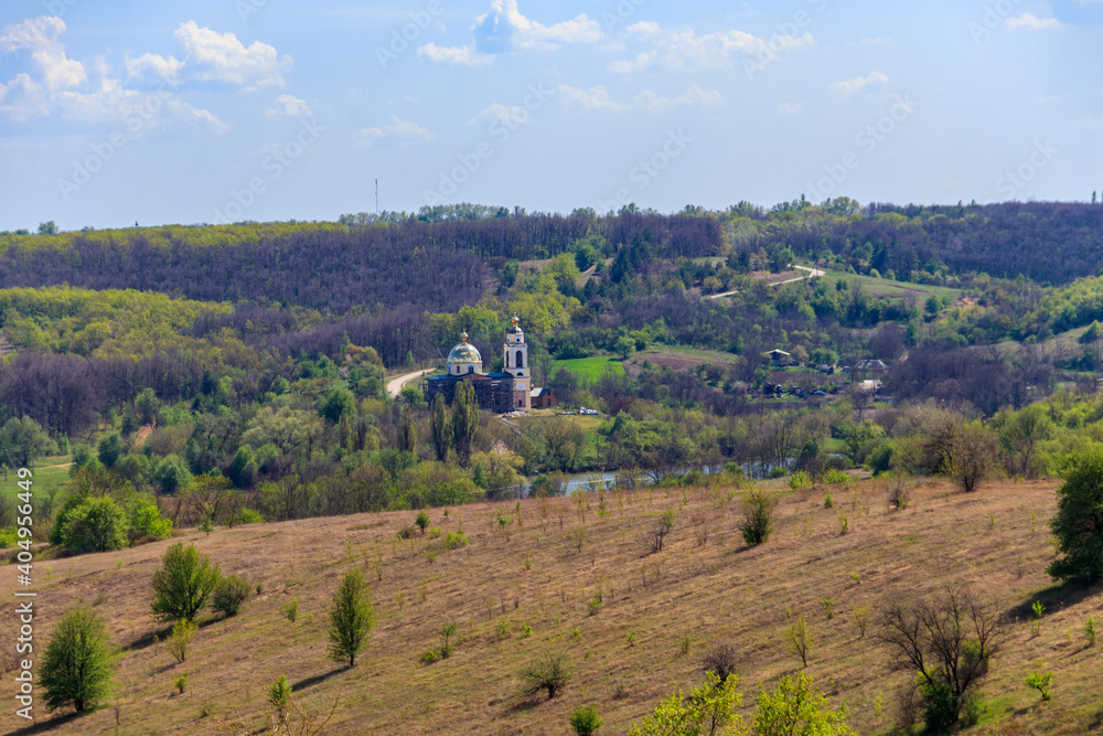 Spring landscape with forest, meadow, hills, lake, small village and orthodox church in Central Ukraine