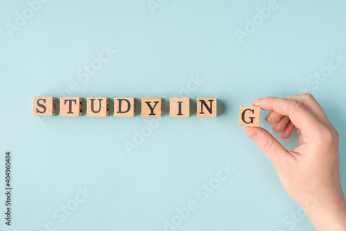 Studying concept. Top above overhead close up flat lay view photo of female hand making word studying putting last block in a single line isolated blue background