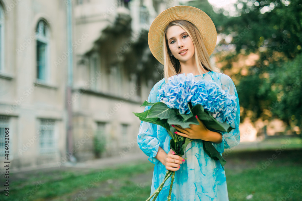 Summer portrait of a beautiful woman walking along the streets with flowers of hydragea