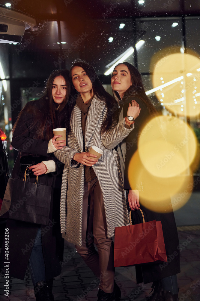Cups of drink in hands. Three cheerful women spends Christmas holidays together outdoors. Conception of new year