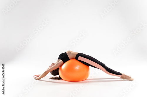 A slender girl in leggings and a sports top lies on a fitness ball on a white isolated background. Athlete girl on a white isolated background, with a fitness ball.