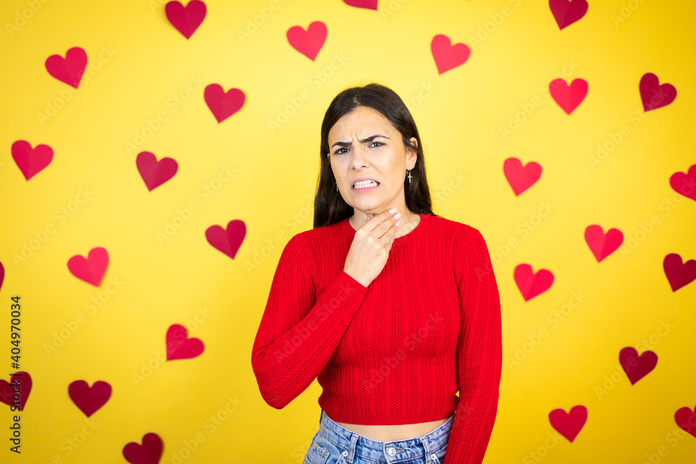 Young caucasian woman over yellow background with red hearts touching painful neck, sore throat for flu, clod and infection Young caucasian woman over yellow background with red hearts touching painful neck, sore throat for flu, clod and infection