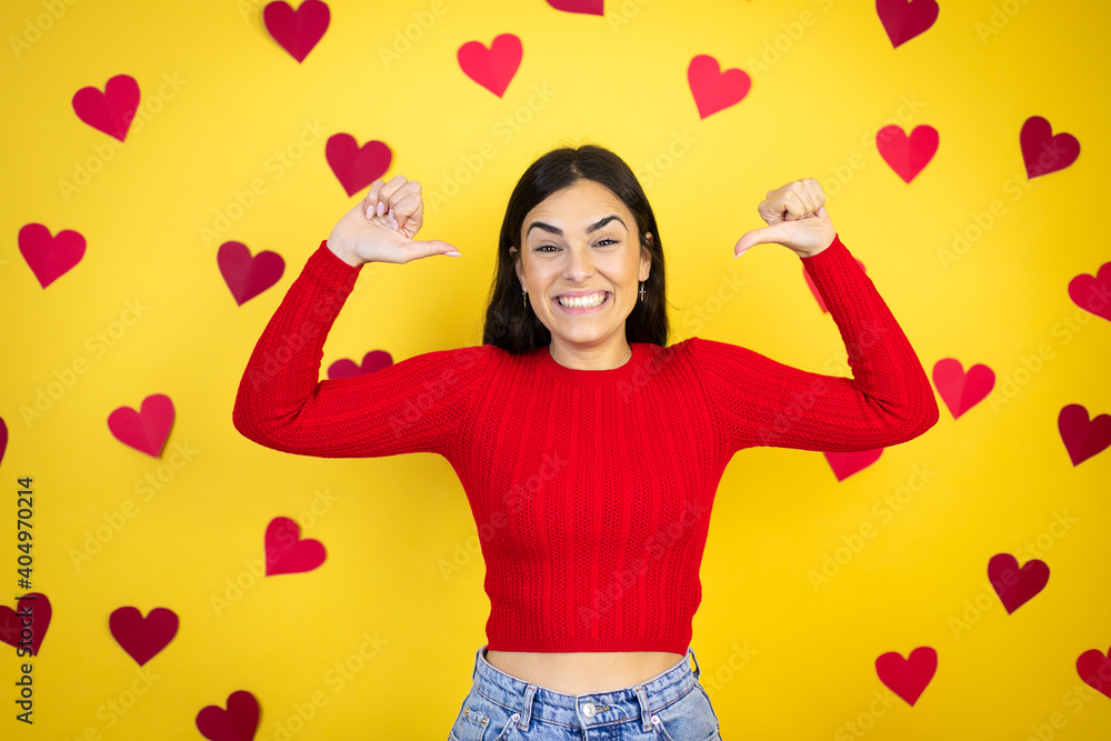 Young caucasian woman over yellow background with red hearts looking confident with smile on face, pointing oneself with fingers proud and happy. Young caucasian woman over yellow background with red hearts looking confident with smile on face, pointing oneself with fingers proud and happy.