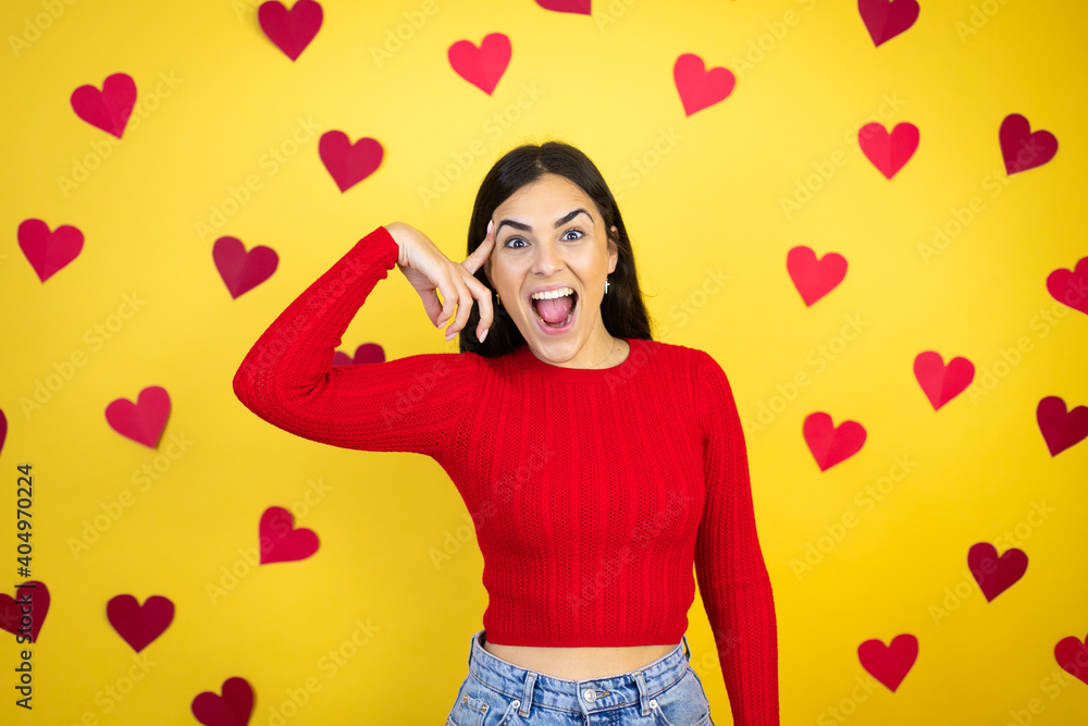 Young caucasian woman over yellow background with red hearts smiling and thinking with her fingers on her head that she has an idea. Young caucasian woman over yellow background with red hearts smiling and thinking with her fingers on her head that she has an idea.