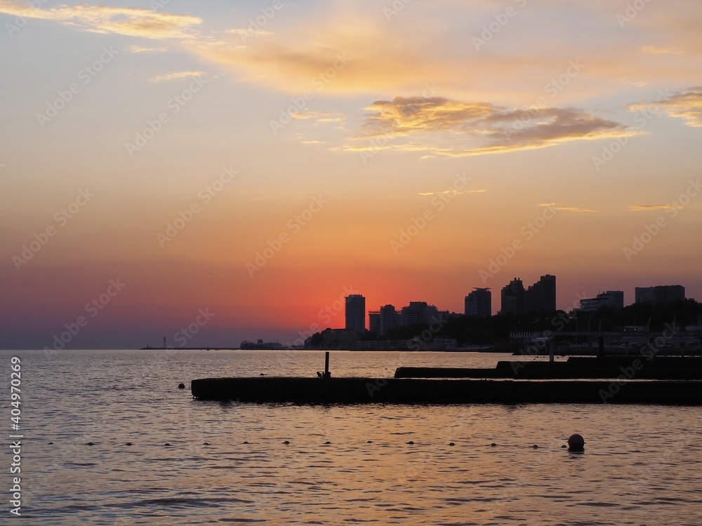 Silhouettes of buildings on the seashore against the background of a bright sunset sky