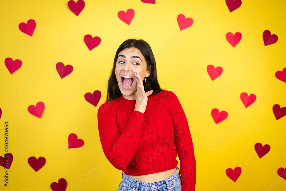 Young caucasian woman over yellow background with red hearts hand on mouth telling secret rumor, whispering malicious talk conversation Young caucasian woman over yellow background with red hearts hand on mouth telling secret rumor, whispering malicious talk conversation