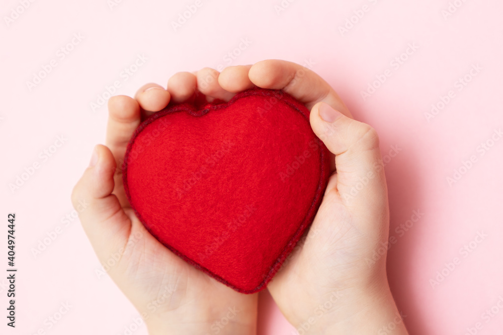 Little child hands holding soft red heart on pink background, close up. Kindness, love and charity concept. Little child hands holding soft red heart on pink background, close up. Kindness, love and charity concept.