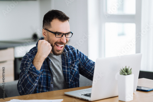 Excited caucasian business man looks at the laptop screen and rejoices because of good news or great deal, happy about well done work, successful project or startup concept