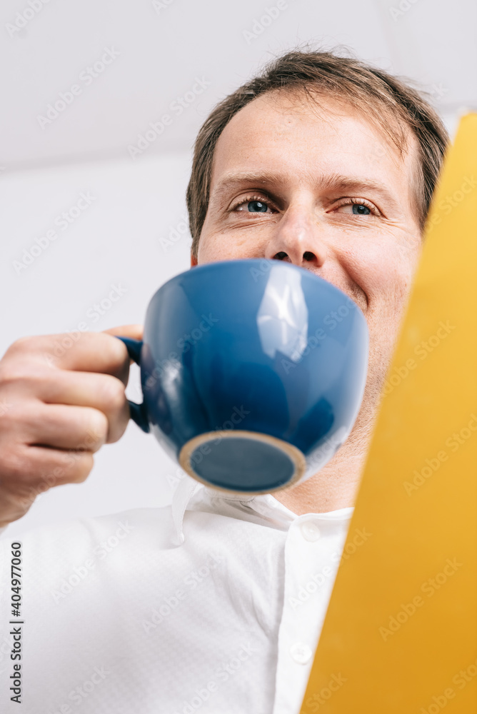 Young man looking at a yellow folder drinking coffee Young man looking at a yellow folder drinking coffee
