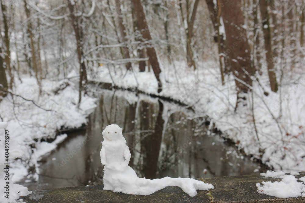 Funny snow sculpture, one day before thaw. Creative miniature snow mermaid as alternative snowman in front of river .