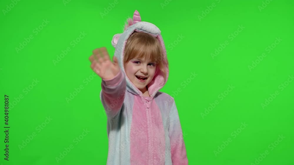 Hello or bye. Little smiling blonde child girl 5-6 years old in unicorn costume posing waving greeting with hand isolated on chroma key green background. Kid animator in unicorn pajamas. Slow motion Hello or bye. Little smiling blonde child girl 5-6 years old in unicorn costume posing waving greeting with hand isolated on chroma key green background. Kid animator in unicorn pajamas. Slow motion