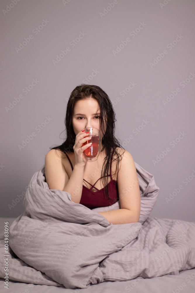 charming sleepy brunette woman with glass cup of tea in bed with grey bed linens. morning routine. charming sleepy brunette woman with glass cup of tea in bed with grey bed linens. morning routine.