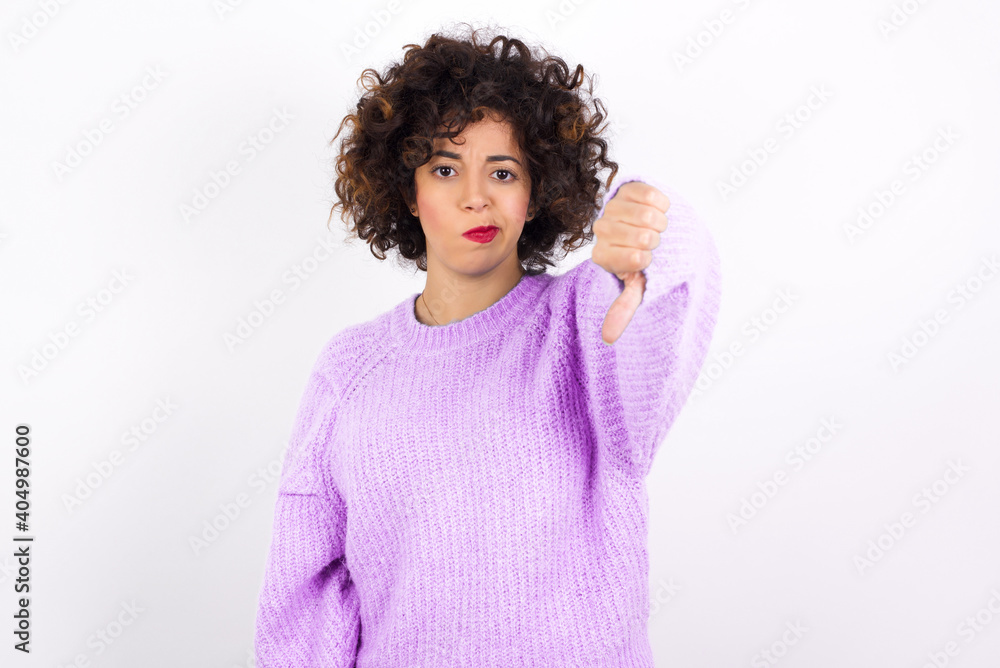 young beautiful caucasian woman wearing pink knitted sweater against white wall looking unhappy and angry showing rejection and negative with thumbs down gesture. Bad expression. young beautiful caucasian woman wearing pink knitted sweater against white wall looking unhappy and angry showing rejection and negative with thumbs down gesture. Bad expression.