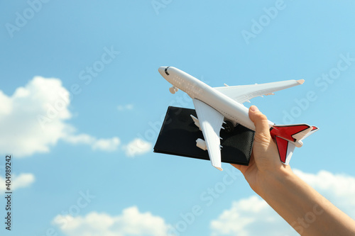 Woman holding toy airplane and passport against blue sky, closeup