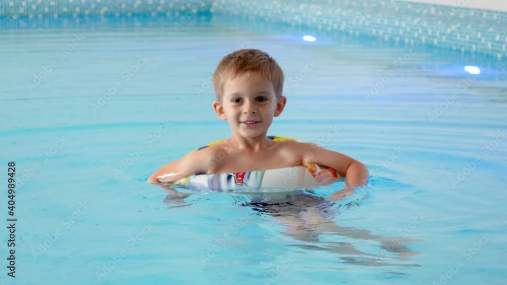 Happy cheerful little boy using inflatable ring while learning swimming in indoor swimming pool at hotel. Happy cheerful little boy using inflatable ring while learning swimming in indoor swimming pool at hotel.