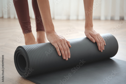 Woman rolling grey yoga mat indoors, closeup © New Africa