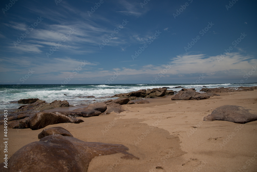 Beautiful sandy ocean beach with large rocks on the shore and in the water