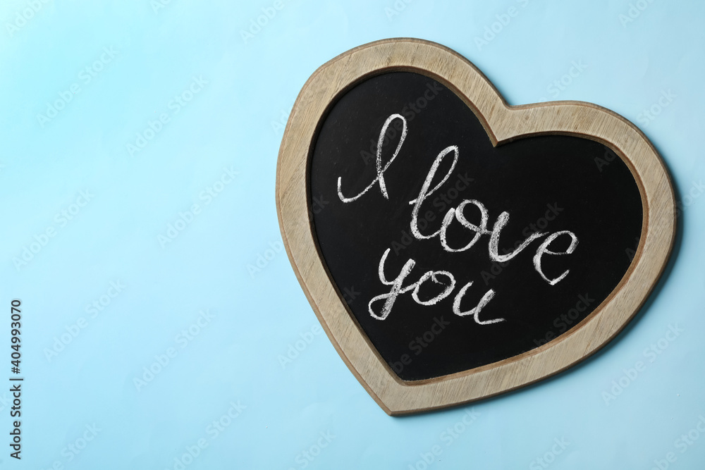 Heart shaped chalkboard with words I Love You on light blue background, top view. Space for text