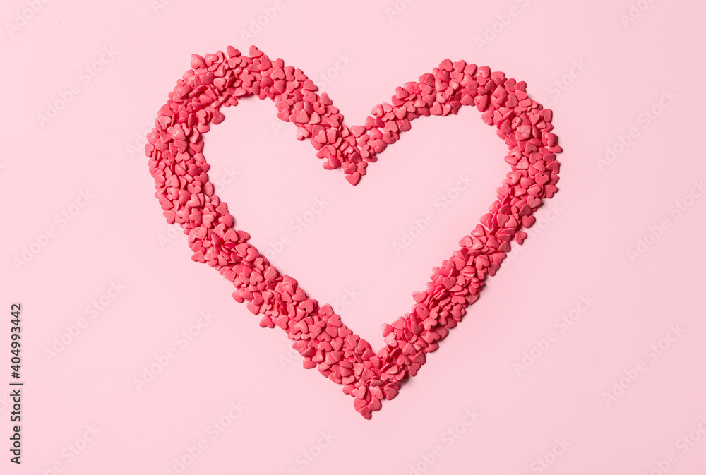 Heart made with sprinkles on pink background, top view