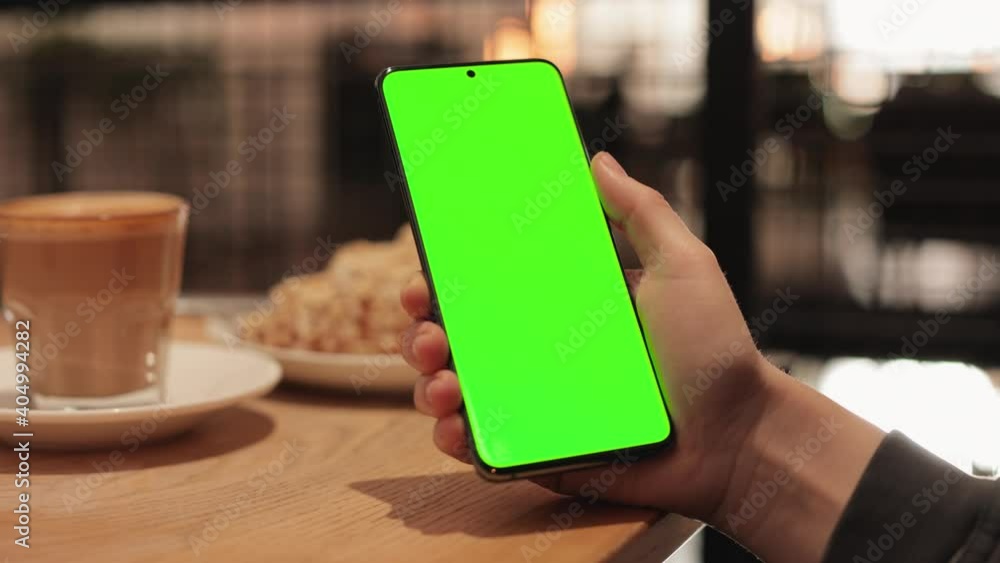 Closeup of Womans Hand is Holding Chroma Key Green Screen in horizontal Position without touching, swiping. Using Phone With Green Mock-up, Surfing Internet, Watching Videos Blogs in Restaurant. Closeup of Womans Hand is Holding Chroma Key Green Screen in horizontal Position without touching, swiping. Using Phone With Green Mock-up, Surfing Internet, Watching Videos Blogs in Restaurant.