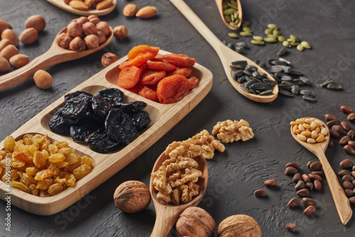 Different kinds of nuts  dried fruits in wooden spoones and dish on black slate background. Top view. Healthy food. Vegetarian nutrition