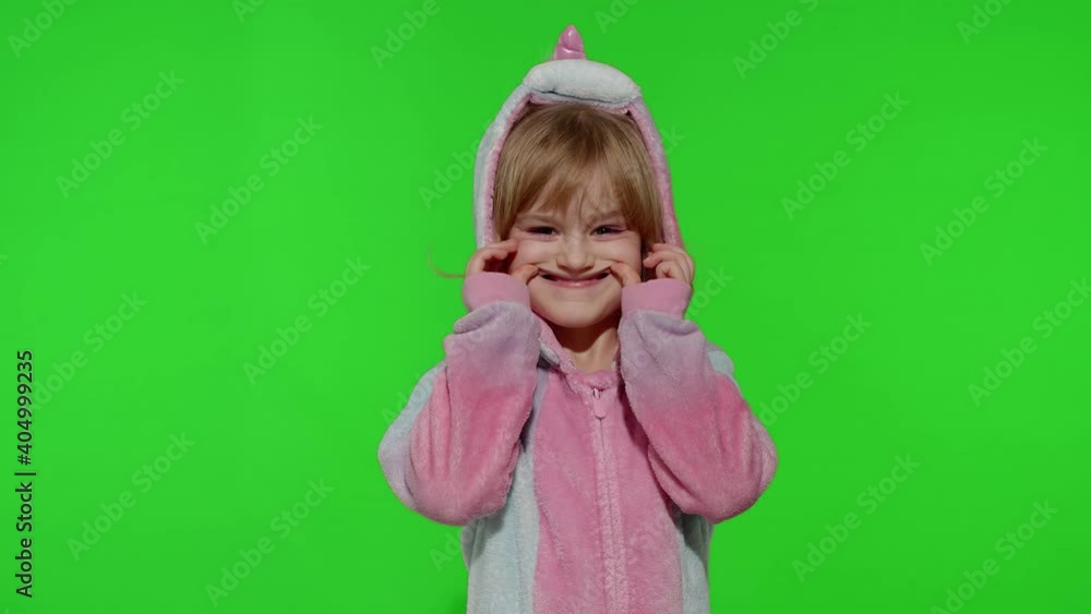 Child making silly funny faces, fooling around, showing tongue. Little teen kid girl in unicorn pajamas posing isolated on chroma key background. People emotions concept. Copy space. Slow motion Child making silly funny faces, fooling around, showing tongue. Little teen kid girl in unicorn pajamas posing isolated on chroma key background. People emotions concept. Copy space. Slow motion
