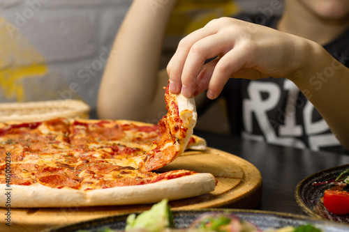 Hand, taking slice of pepperoni pizza from round wooden tray