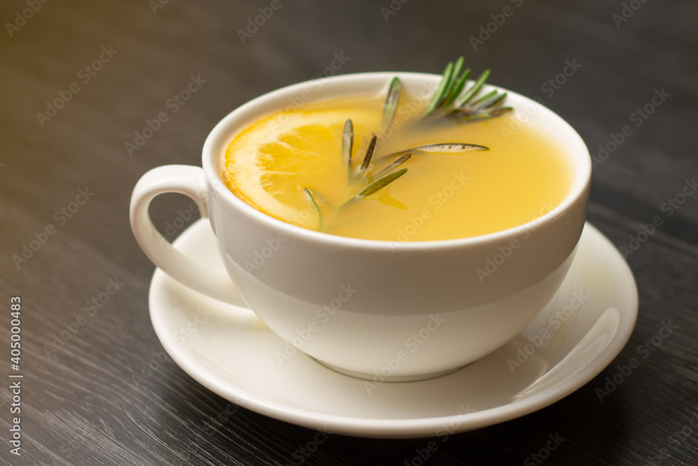 Yellow ginger tea with lemon and rosemary branch, in white cup on wooden table Yellow ginger tea with lemon and rosemary branch, in white cup on wooden table