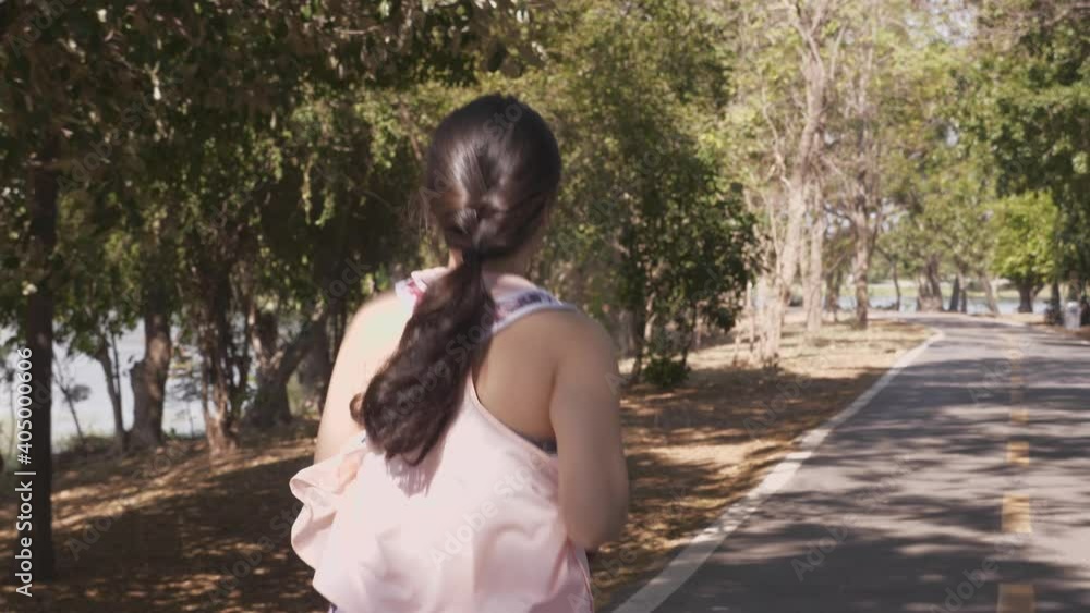 Rear view, medium to close up shot of young woman in sportswear running, jogging at the park, along the shady straight road in the morning. Handheld, outdoor, Asian people and active lifestyle concept Rear view, medium to close up shot of young woman in sportswear running, jogging at the park, along the shady straight road in the morning. Handheld, outdoor, Asian people and active lifestyle concept